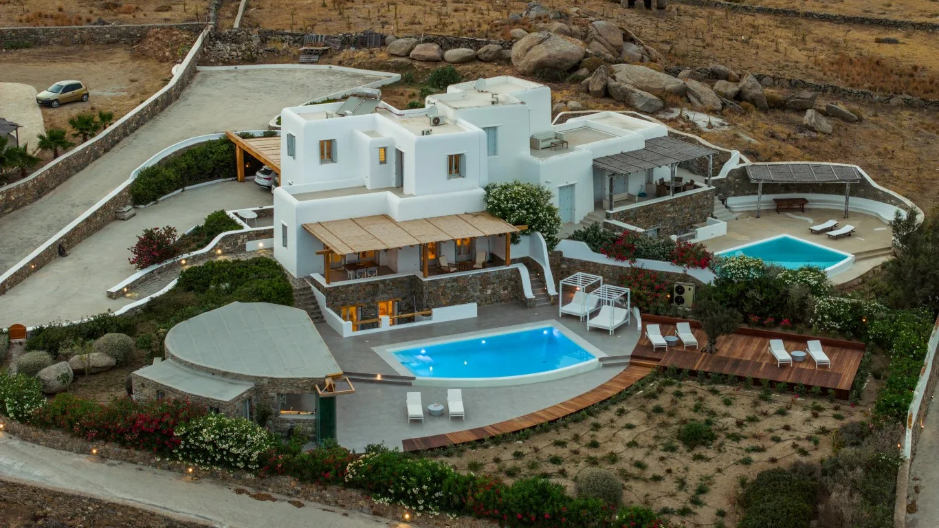 A white villa overlooks a curved swimming pool and landscaped grounds.