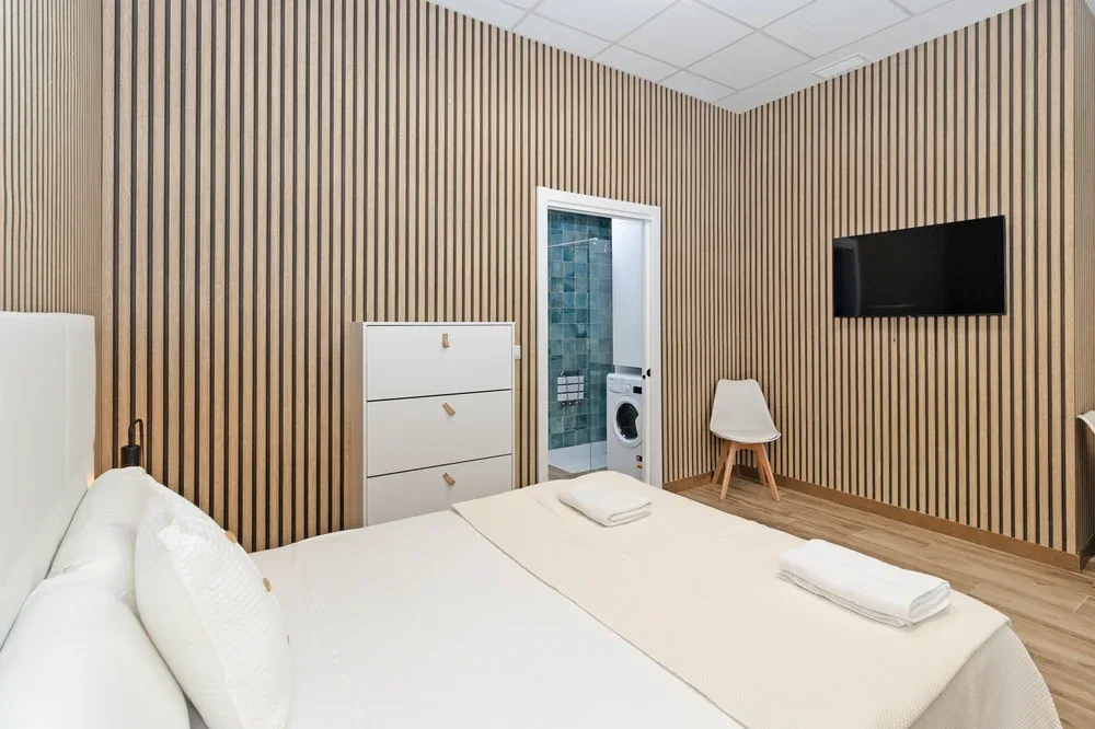 A bedroom with a neatly made bed and a wall-mounted television.