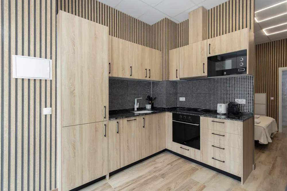 A compact kitchen with light wood cabinetry, dark counters, and a tiled backsplash.