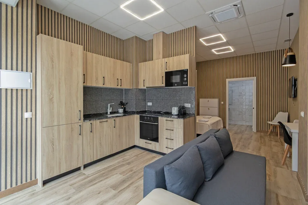 An open-plan kitchen and living area with wood cabinetry and a gray sofa.