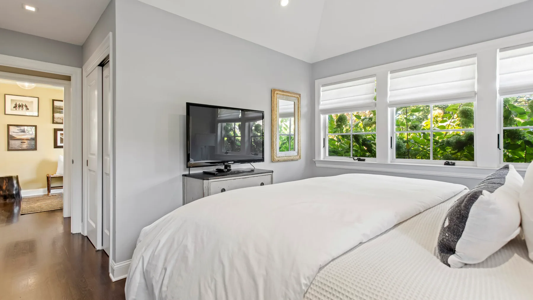 Un dormitorio luminoso tiene una cama grande junto a amplias ventanas con vistas al follaje verde.