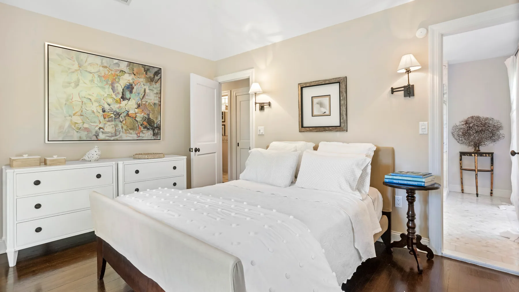 Un dormitorio con una cama blanca, una cómoda y cuadros en la pared.
