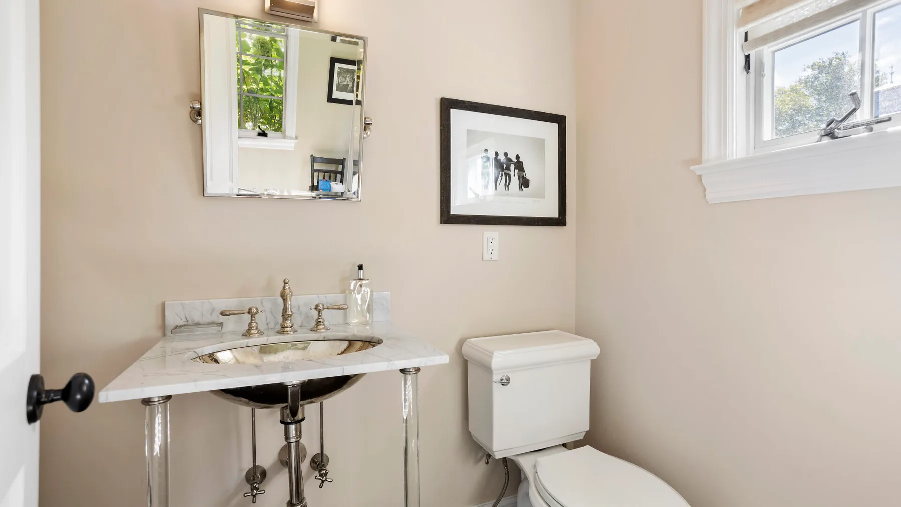 Un baño con lavabo de pedestal e inodoro bajo una ventana.