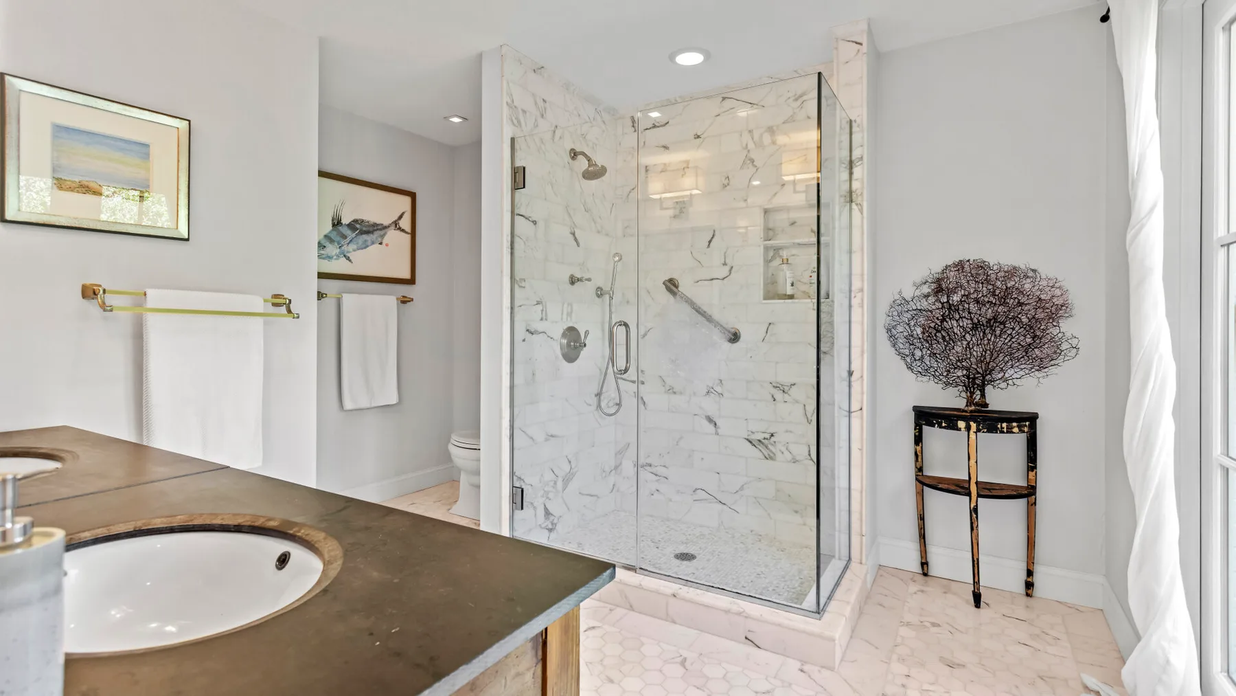 Un baño luminoso con una ducha de azulejos marmoleados y un lavabo.