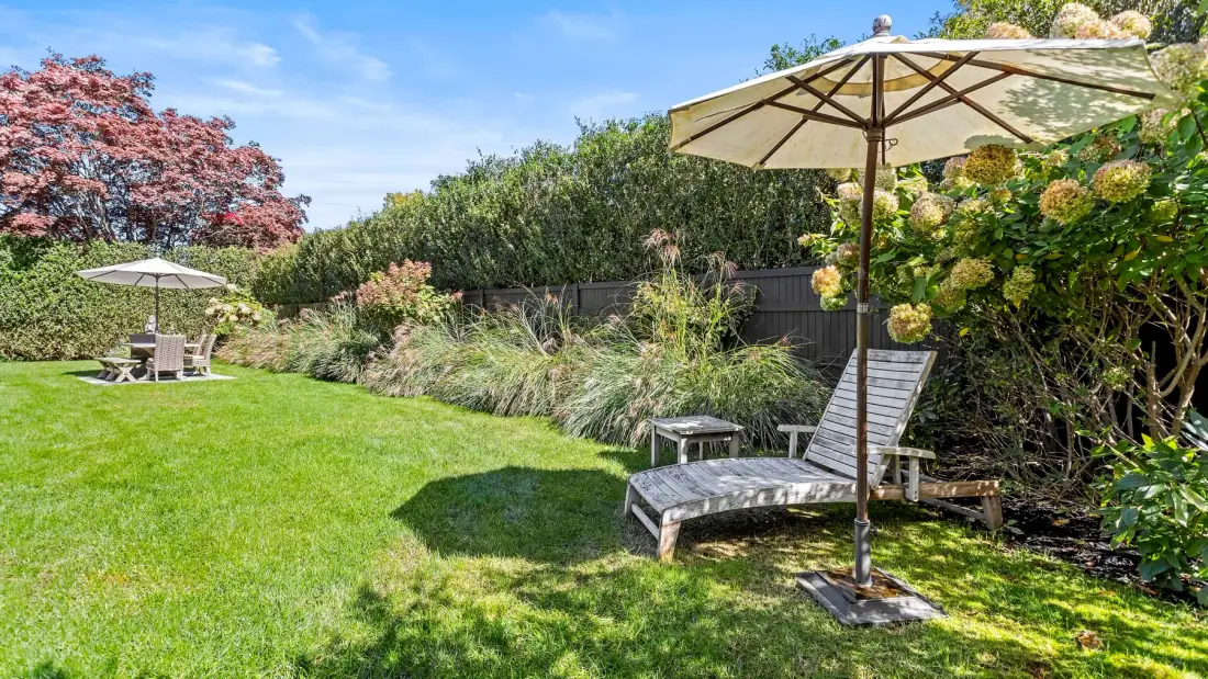 Un jardín cuidado con césped, asientos al aire libre y sombrillas.