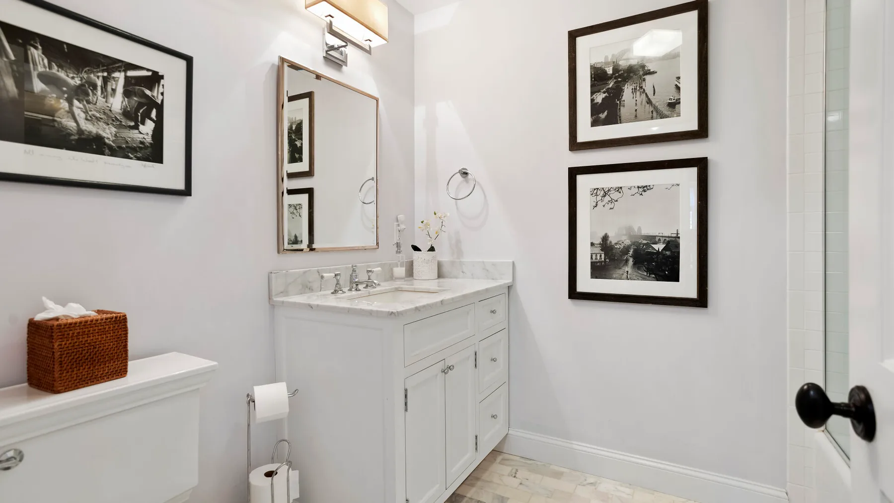 Un baño luminoso con un tocador blanco, un espejo y cuadros en la pared.
