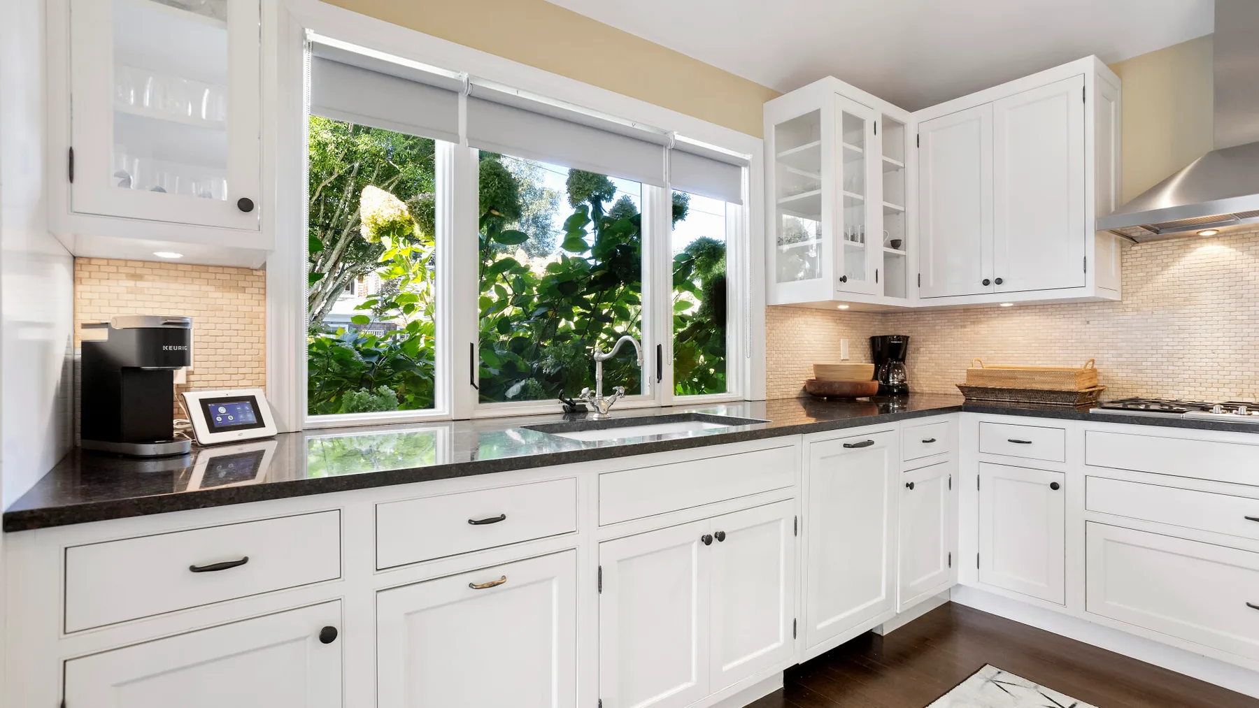 Una cocina luminosa con gabinetes blancos, encimeras oscuras y una ventana grande.