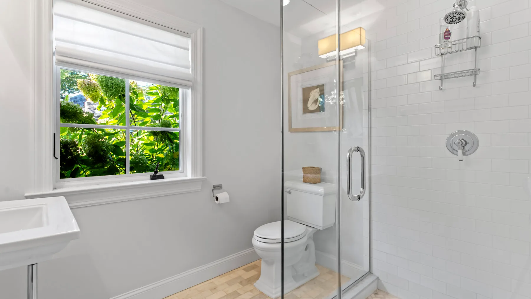 Un baño luminoso con ducha de vidrio, inodoro y una ventana con vista a la vegetación.