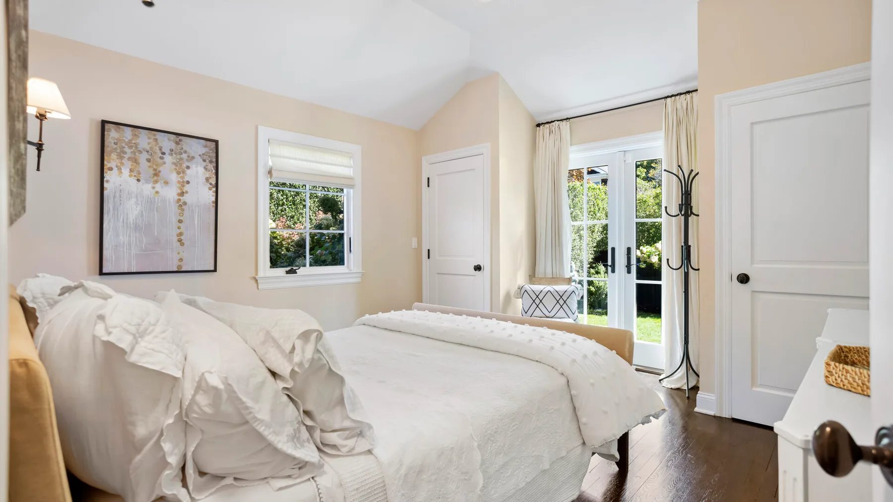 Un dormitorio luminoso con una cama blanca y una ventana junto a puertas de vidrio.
