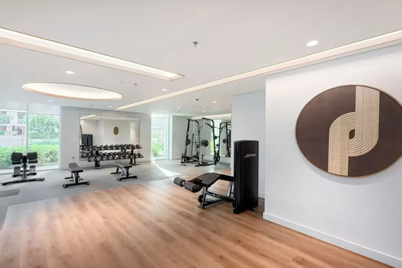 Un gimnasio luminoso con equipos de ejercicio, pesas y ventanas grandes.