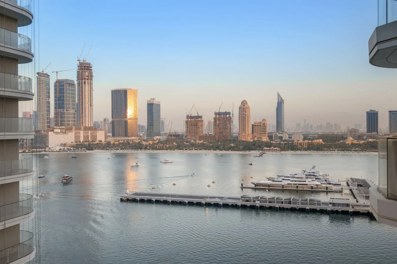 Un horizonte urbano se alza junto a una bahía tranquila, con barcos y una marina en primer plano.