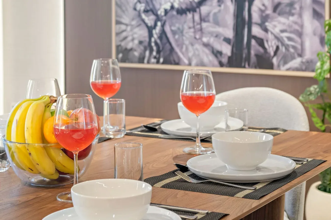 Una mesa de comedor está preparada con platos, copas y un frutero.