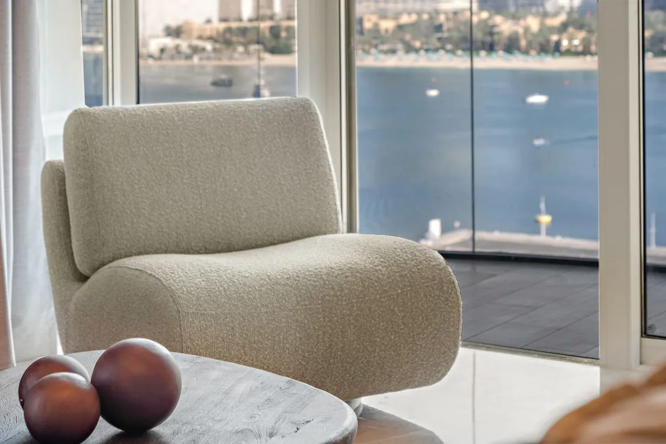 Una luminosa sala de estar con un asiento curvo tapizado junto a grandes ventanas con vistas al agua.
