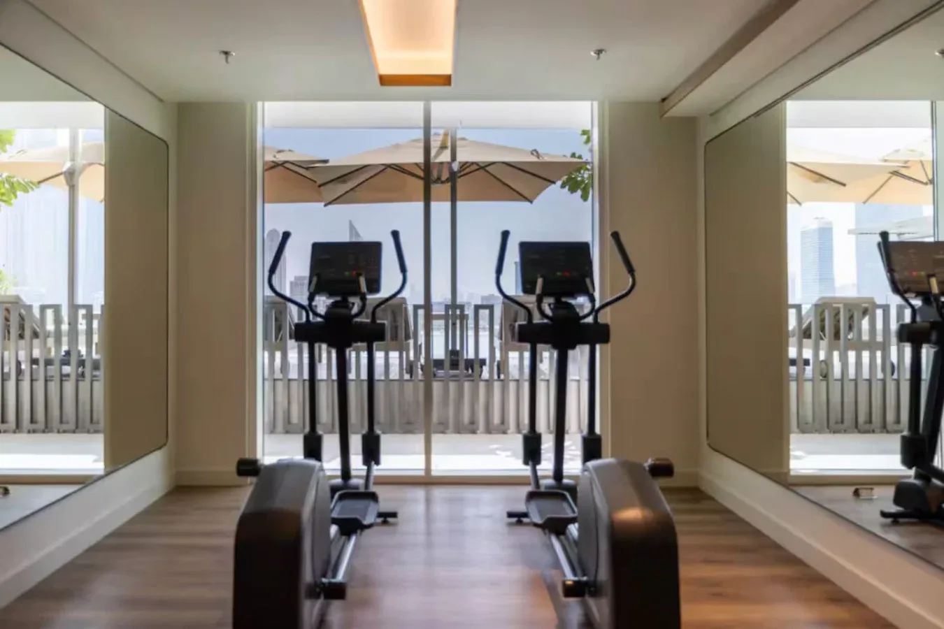 Un pequeño gimnasio con máquinas de ejercicio frente a una puerta de vidrio que da a un patio exterior.
