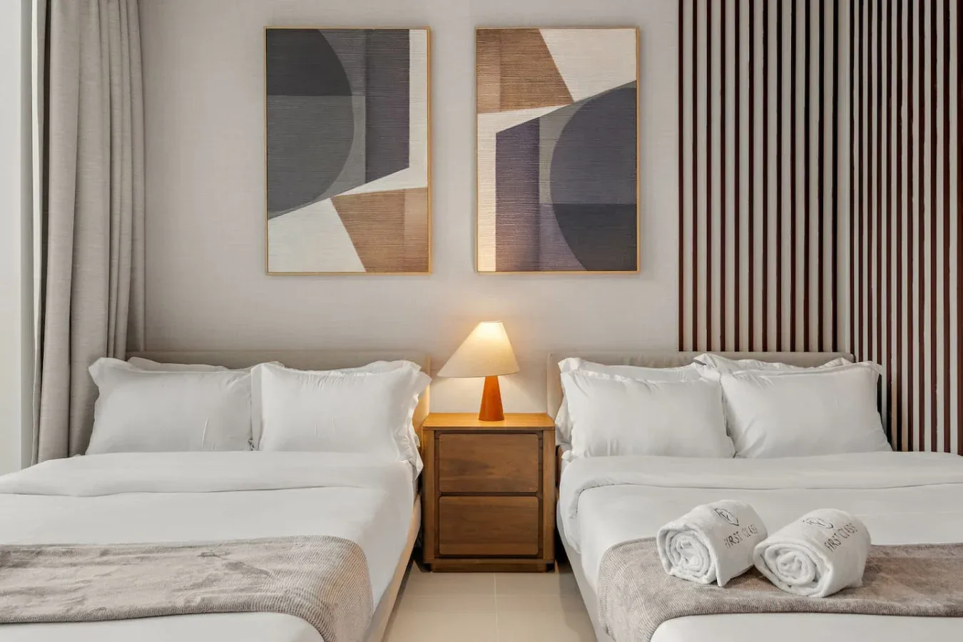 Un dormitorio con dos camas, ropa de cama blanca y una lámpara encendida.