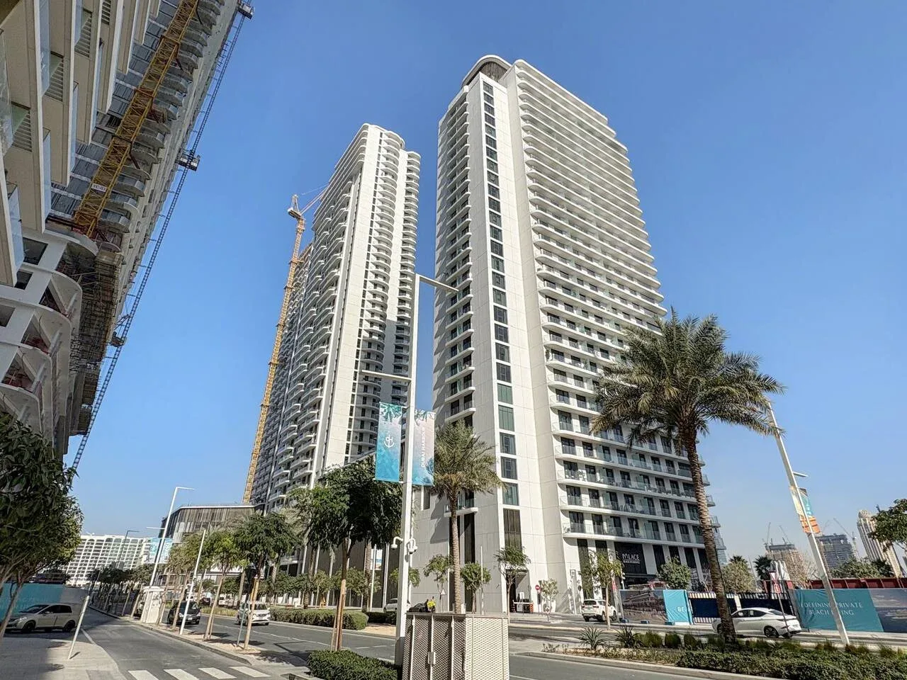 Torres residenciales altas se alzan junto a una calle urbana bordeada de palmeras.