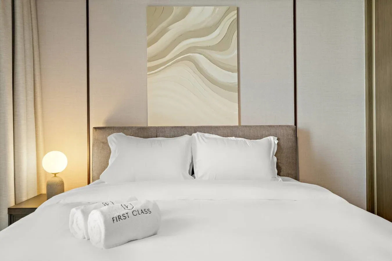Una cama bien tendida con ropa de cama blanca y arte abstracto sobre el cabecero.