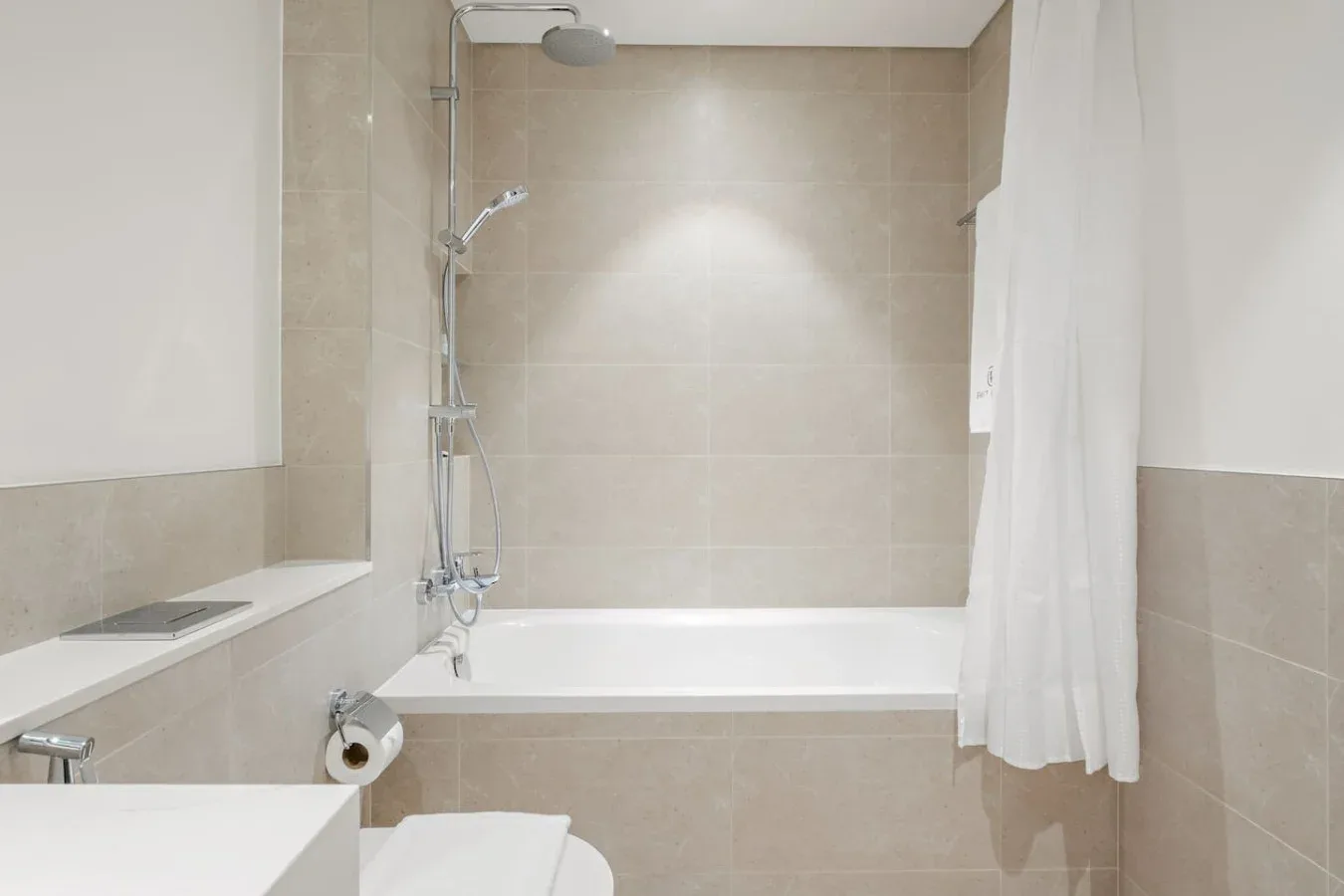 Un baño alicatado con bañera, ducha y cortina blanca.