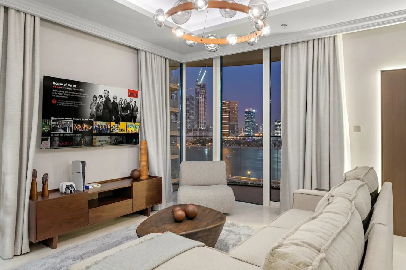 Una sala de estar con asientos y grandes ventanales con vistas a la ciudad al anochecer.