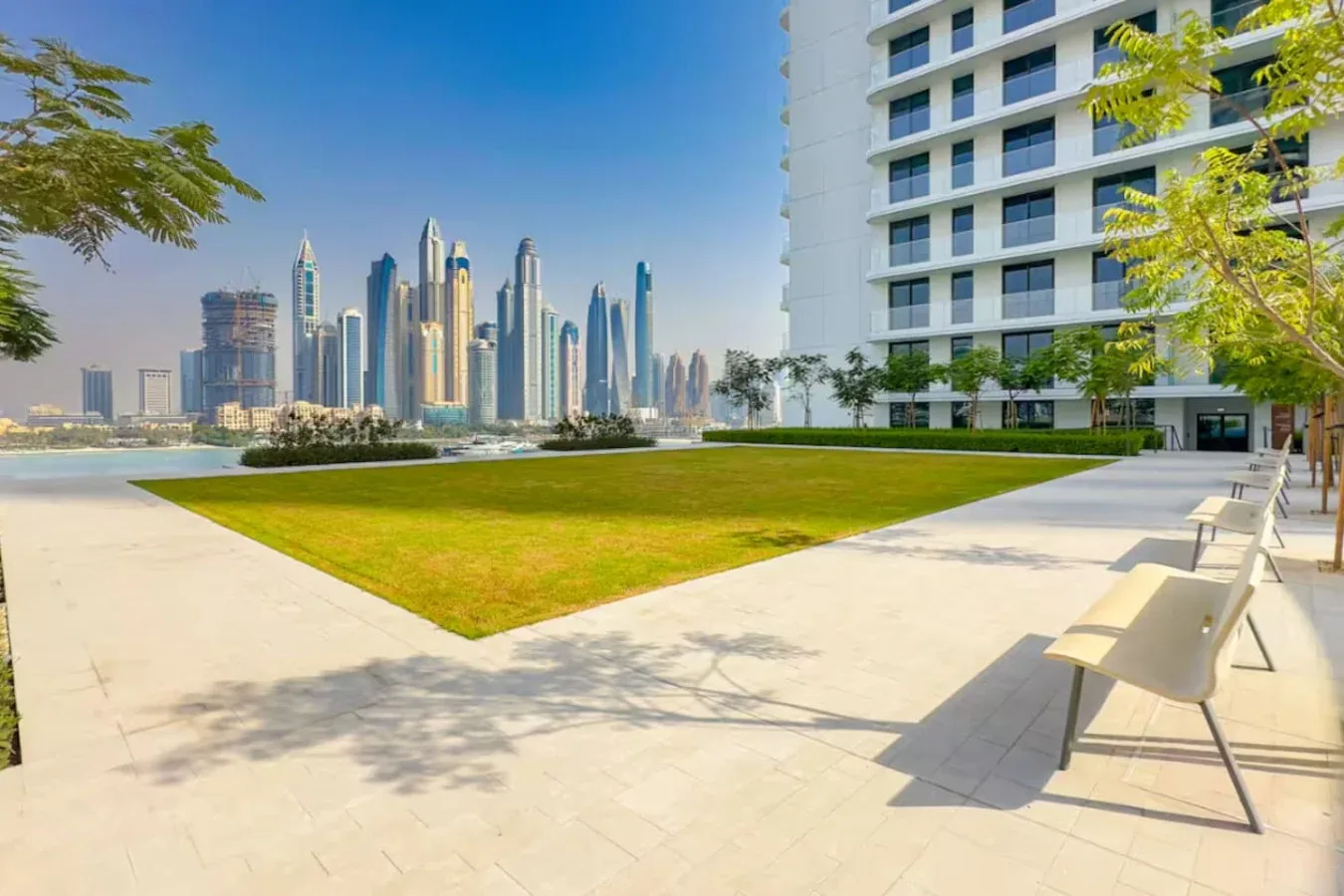 Un patio ajardinado con césped, asientos y un horizonte urbano al fondo.