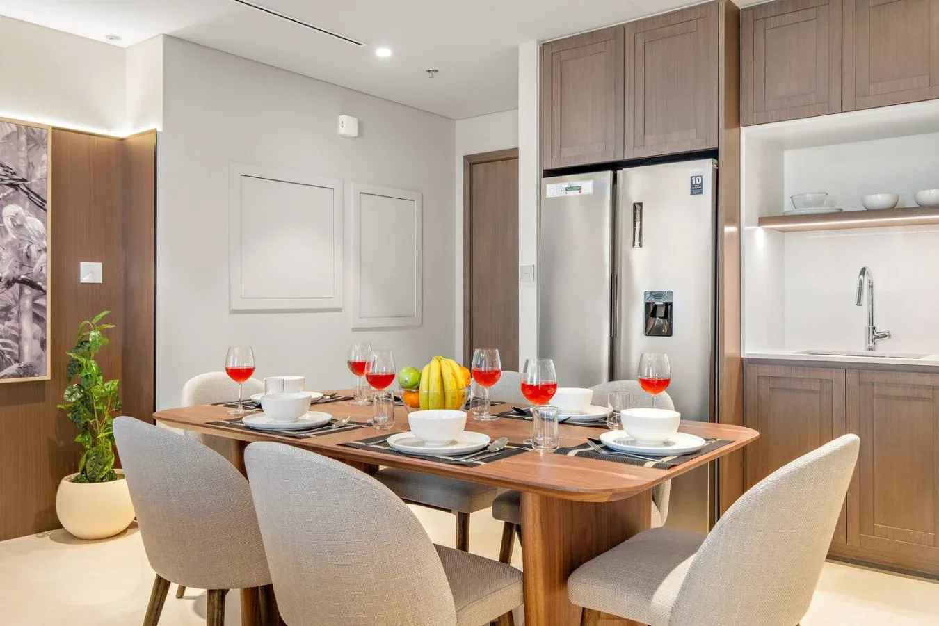 Una mesa preparada para comer está junto a una cocina con refrigerador y fregadero.