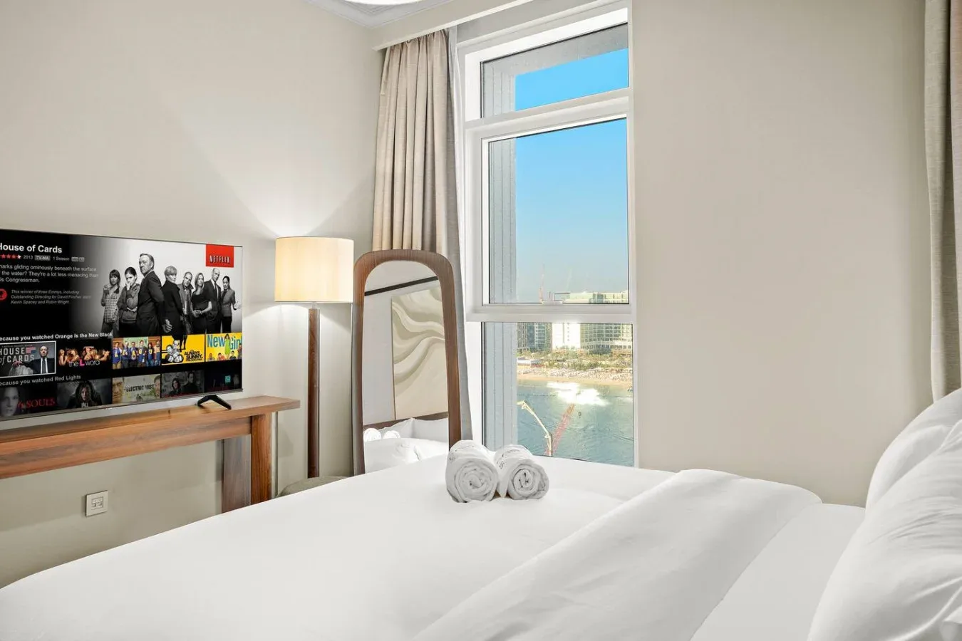 Un dormitorio luminoso con una cama arreglada junto a una ventana con vistas al agua.