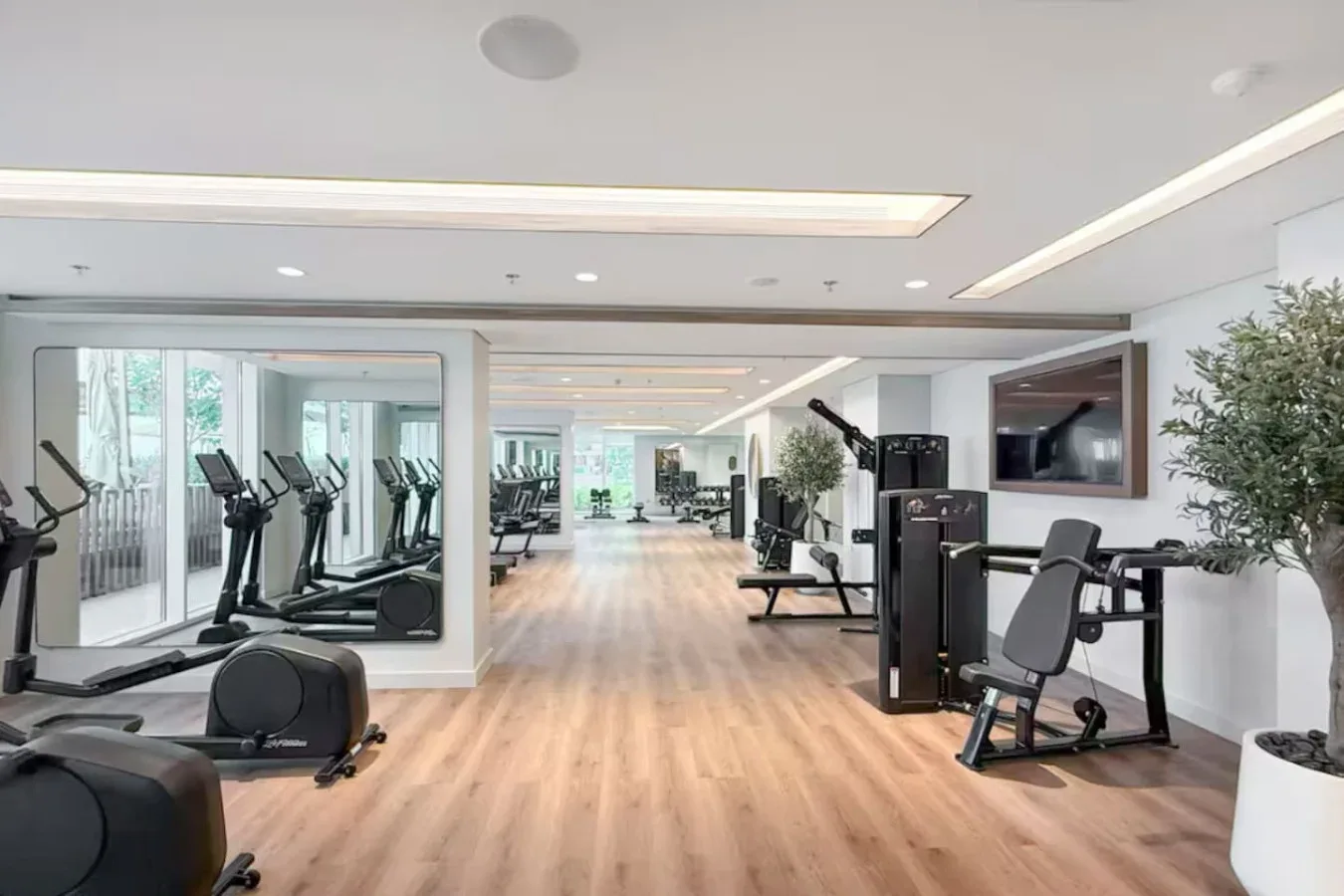 Una sala de fitness luminosa con máquinas de ejercicio y suelo de madera clara.