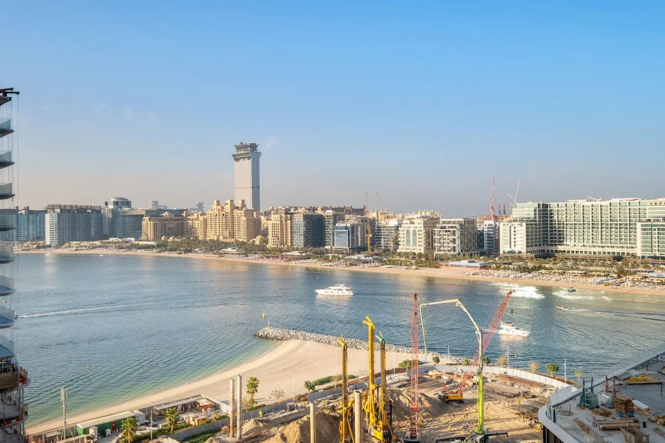 Una bahía costera con playa de arena, edificios frente al agua y obras en primer plano.