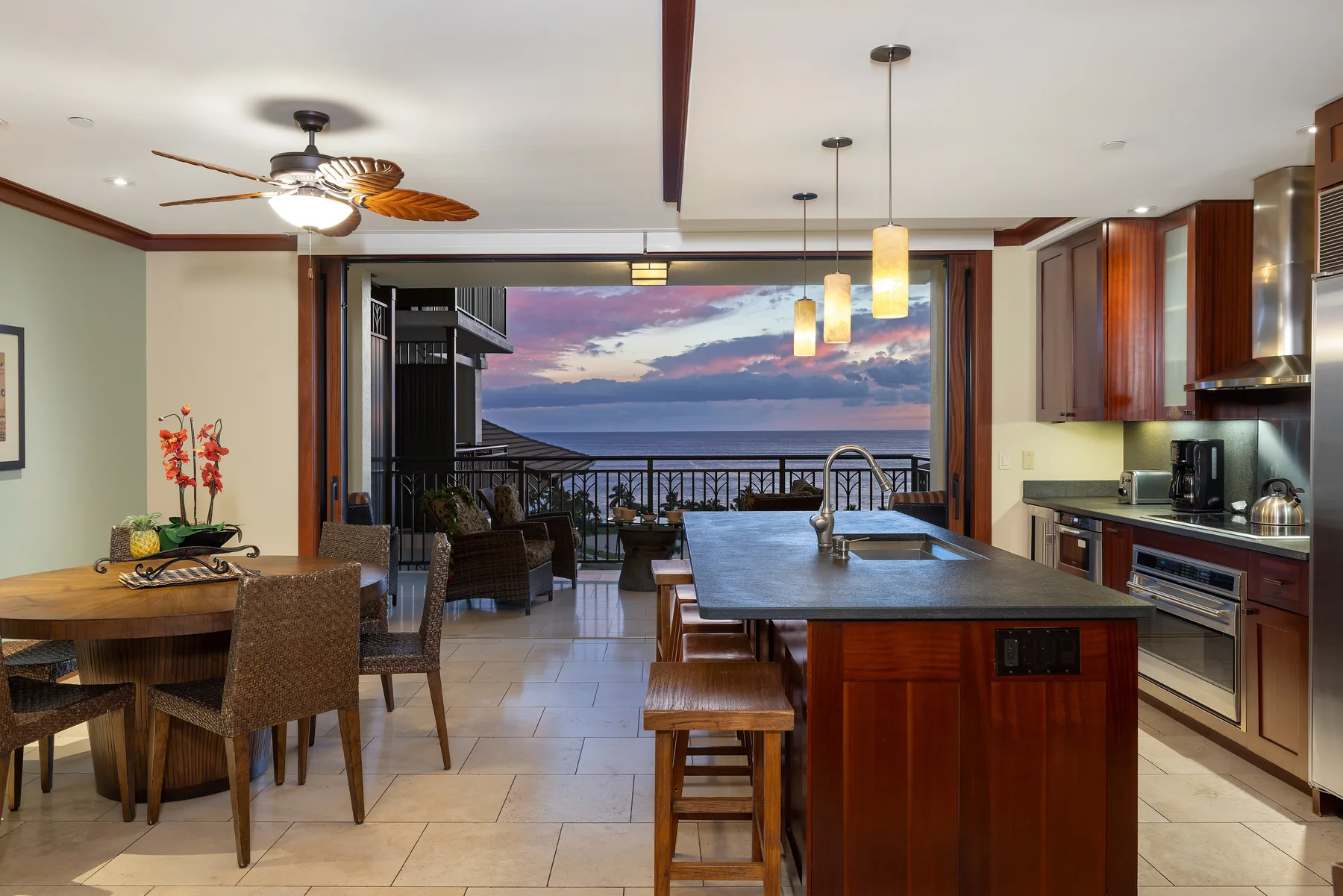 Una cocina abierta y comedor tienen vistas al océano al atardecer.