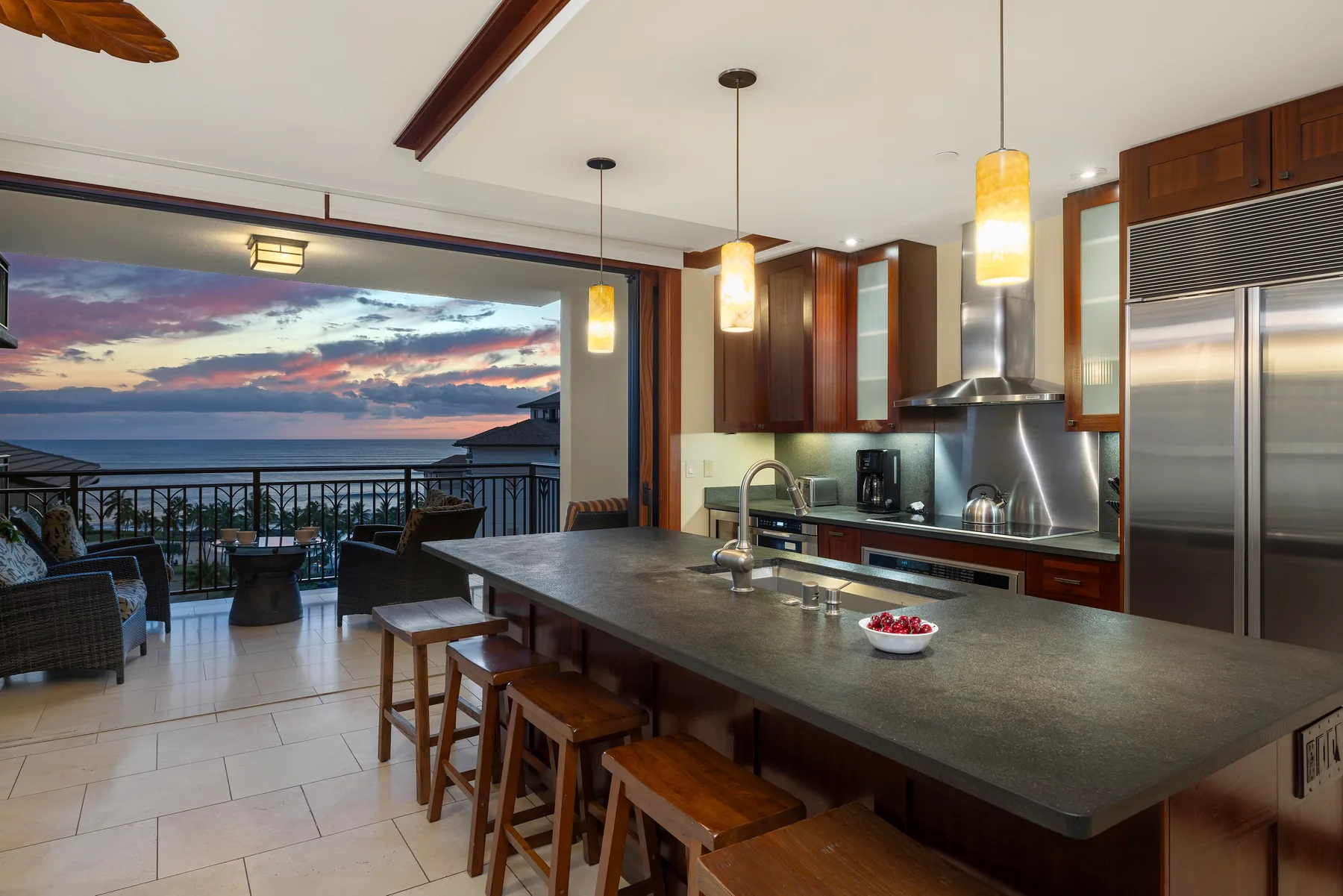Una cocina con una gran isla se abre a un balcón con vistas al océano al atardecer.