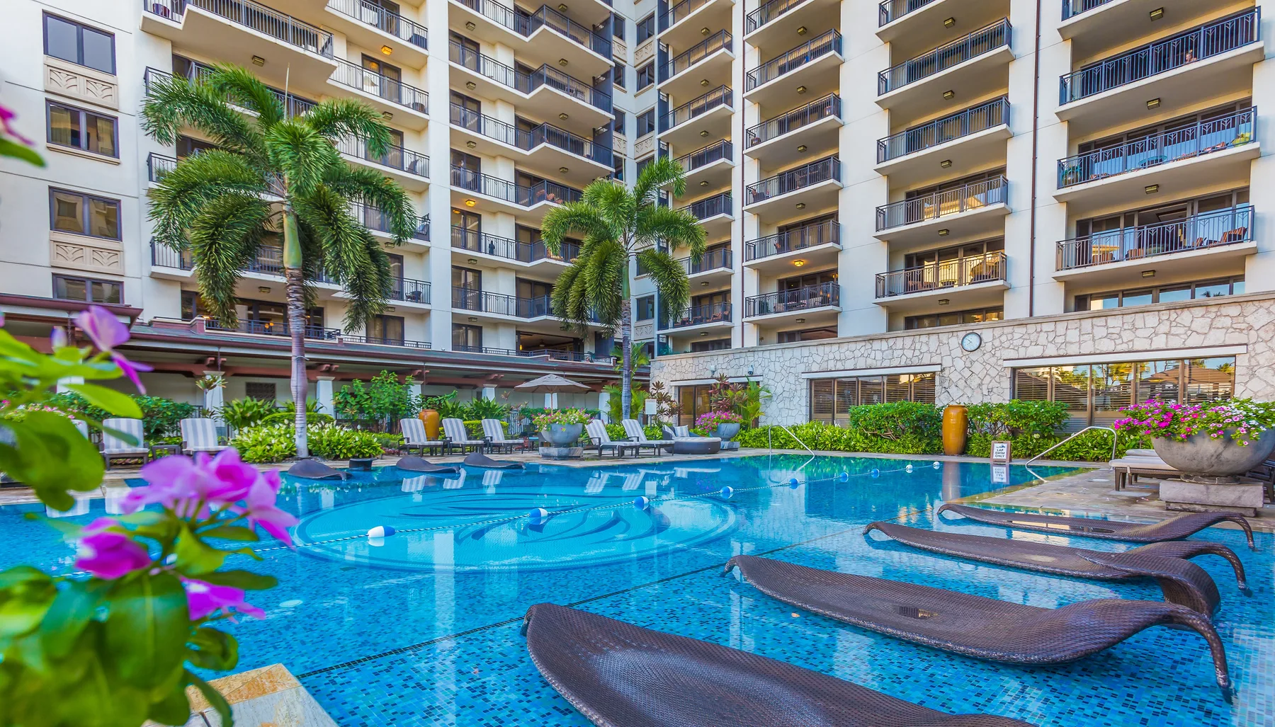 Una piscina rodeada de balcones de apartamentos y plantas tropicales.