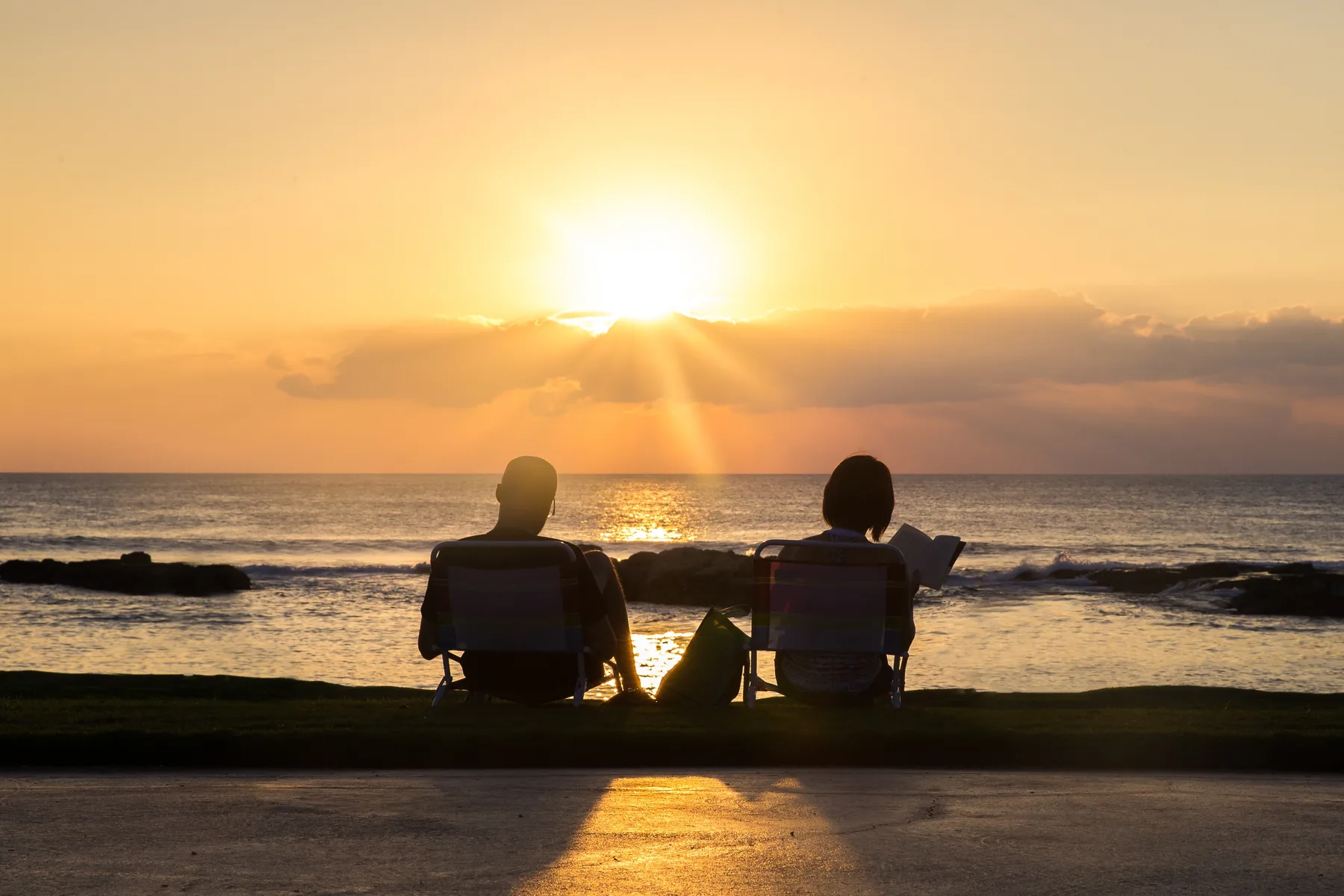 Dos personas se sientan frente al océano mientras el sol se pone sobre el agua.