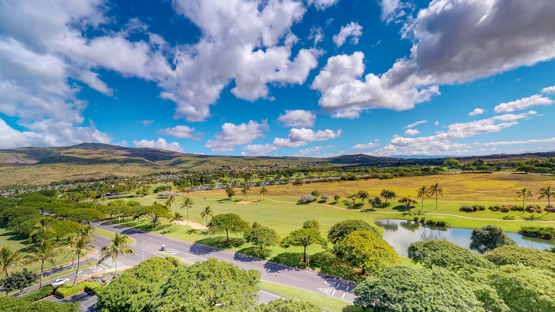 Un amplio paisaje verde con una carretera sinuosa, estanques y colinas bajo un cielo nublado.