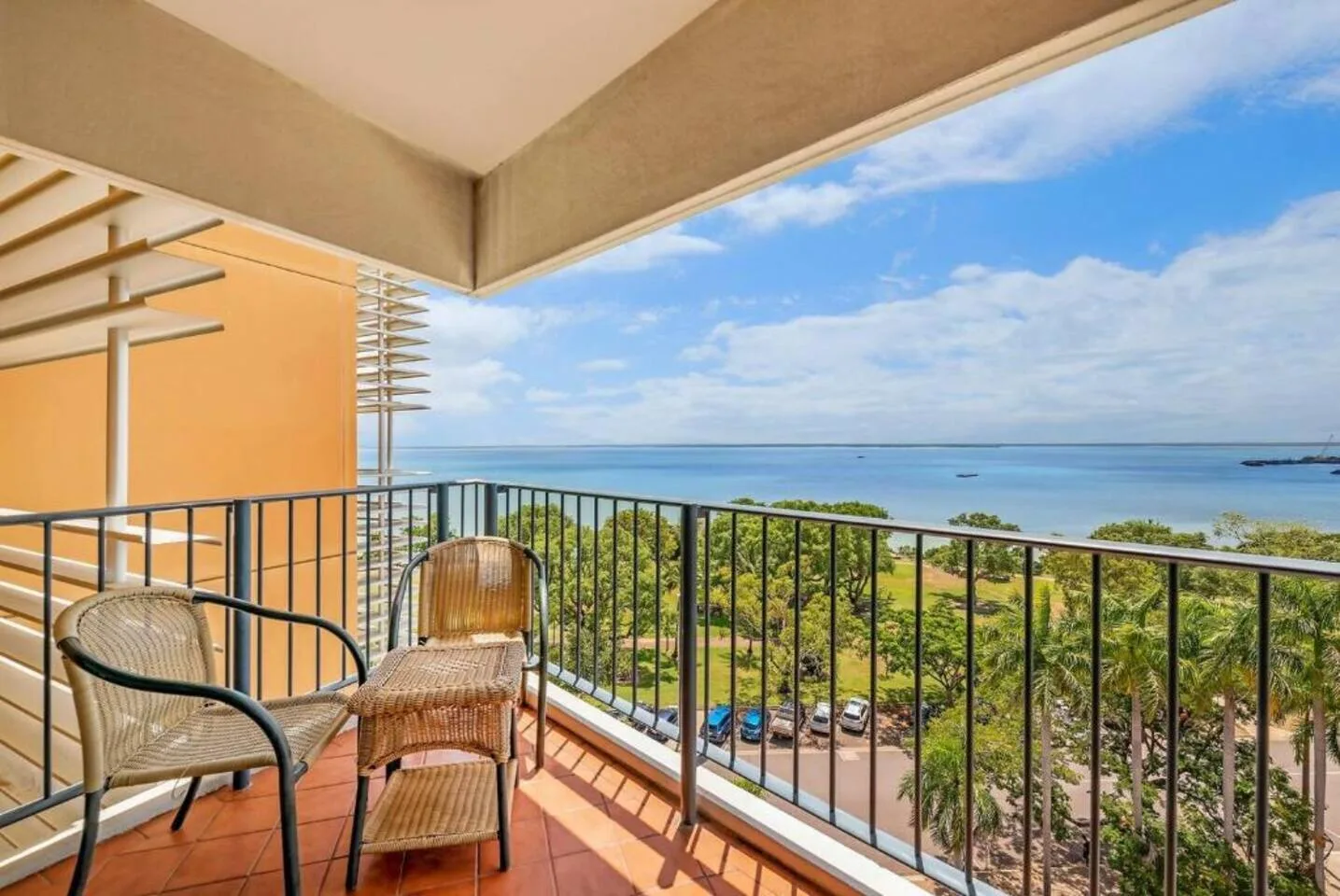 A covered balcony with seating overlooks the sea and a tree-lined shoreline.