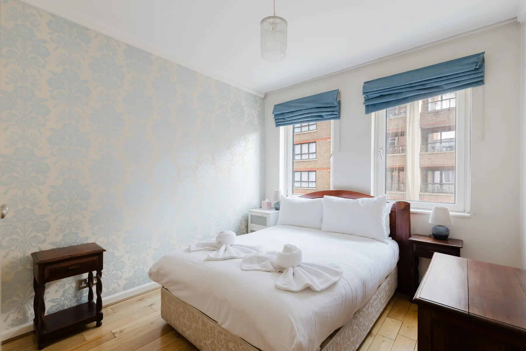 A bedroom with a bed beneath two windows and blue blinds.