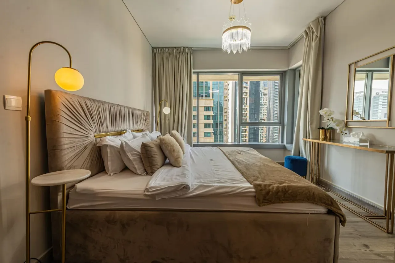 A bedroom with a large bed and windows overlooking nearby buildings.