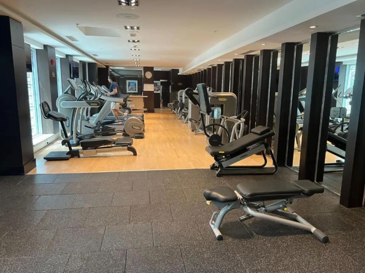 Un gimnasio con máquinas de ejercicio y bancos de pesas distribuidos por la sala.