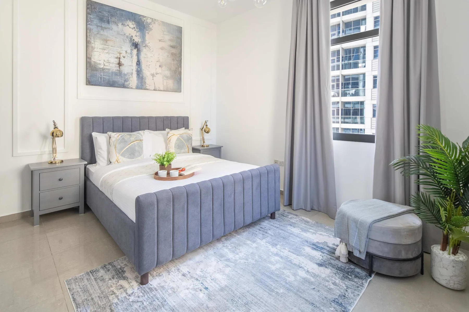 Un dormitorio luminoso con una cama, una ventana grande y cortinas grises.