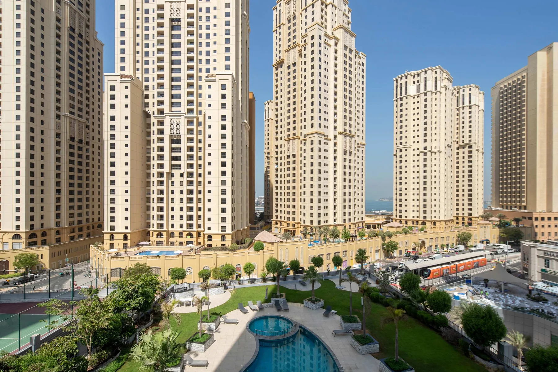 Un patio ajardinado con una piscina curva está rodeado de altas torres residenciales.
