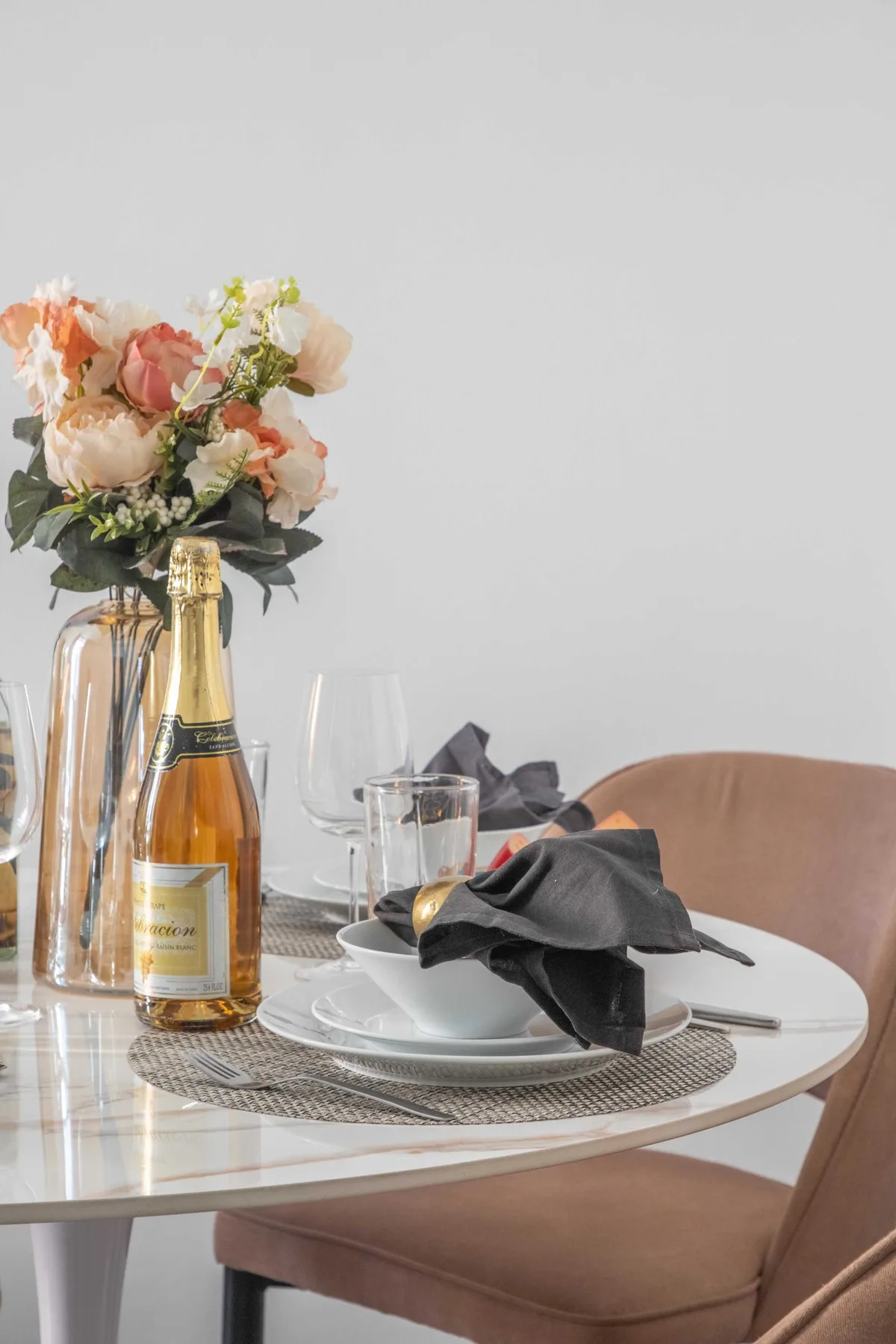 Una mesa de comedor está preparada con platos, servilletas dobladas y una botella junto a flores.