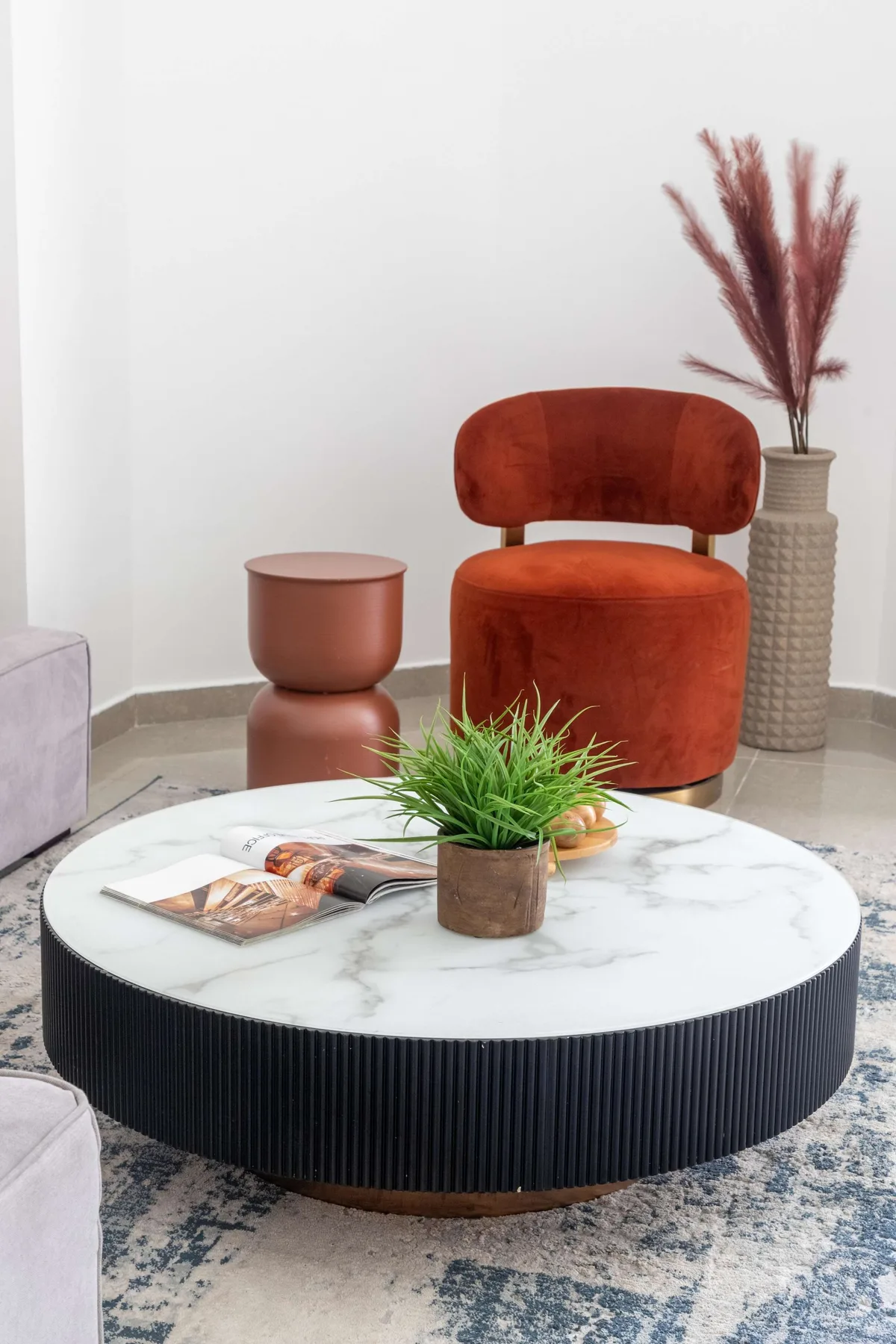 Una zona de estar con un sillón color óxido y una mesa de centro redonda.