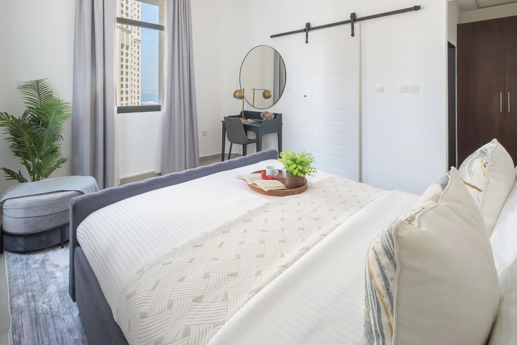 Un dormitorio luminoso con una cama tendida y un pequeño escritorio junto a la ventana.