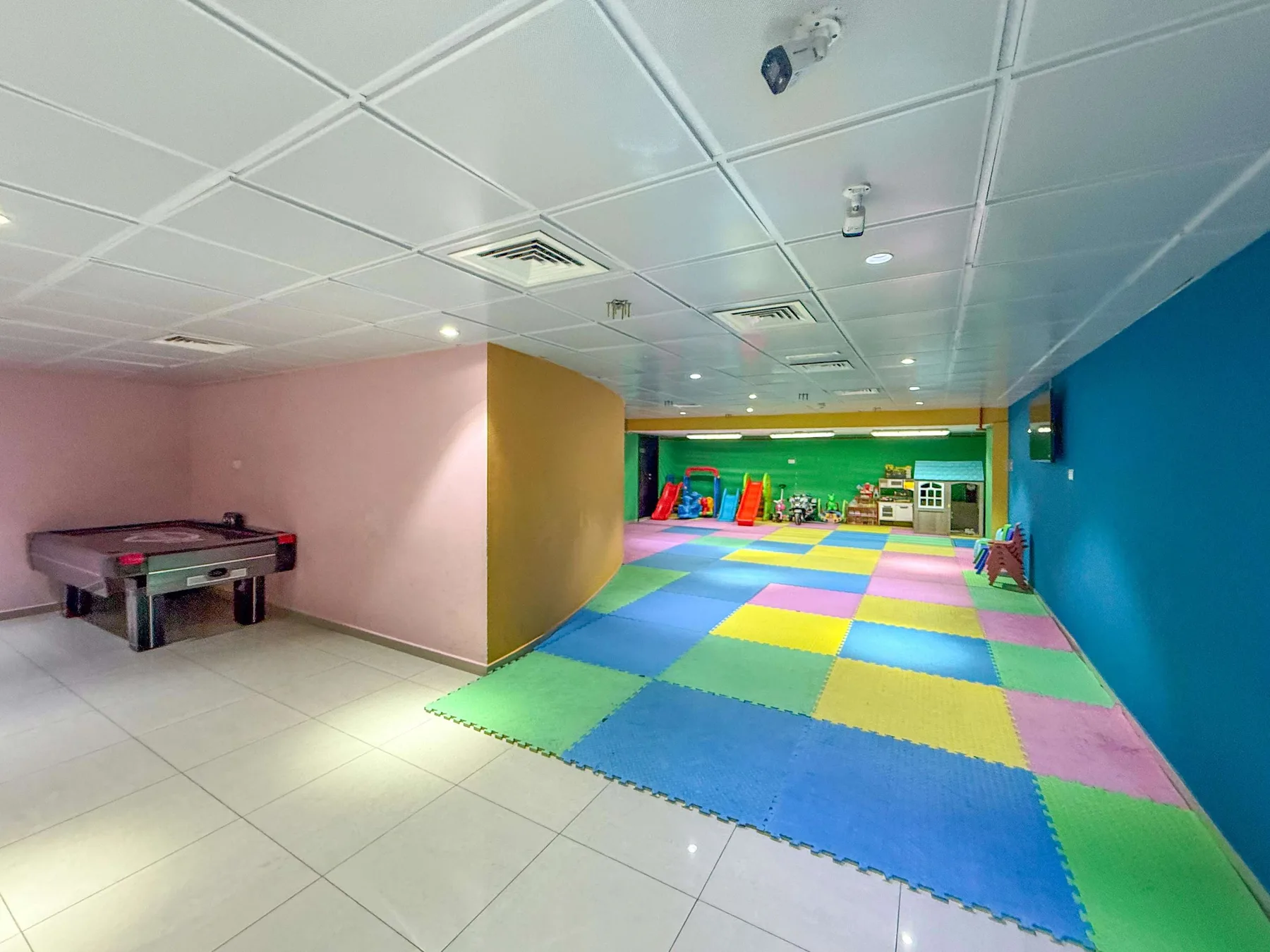 Un área de juegos interior colorida con suelo acolchado y un juego de mesa pequeño.