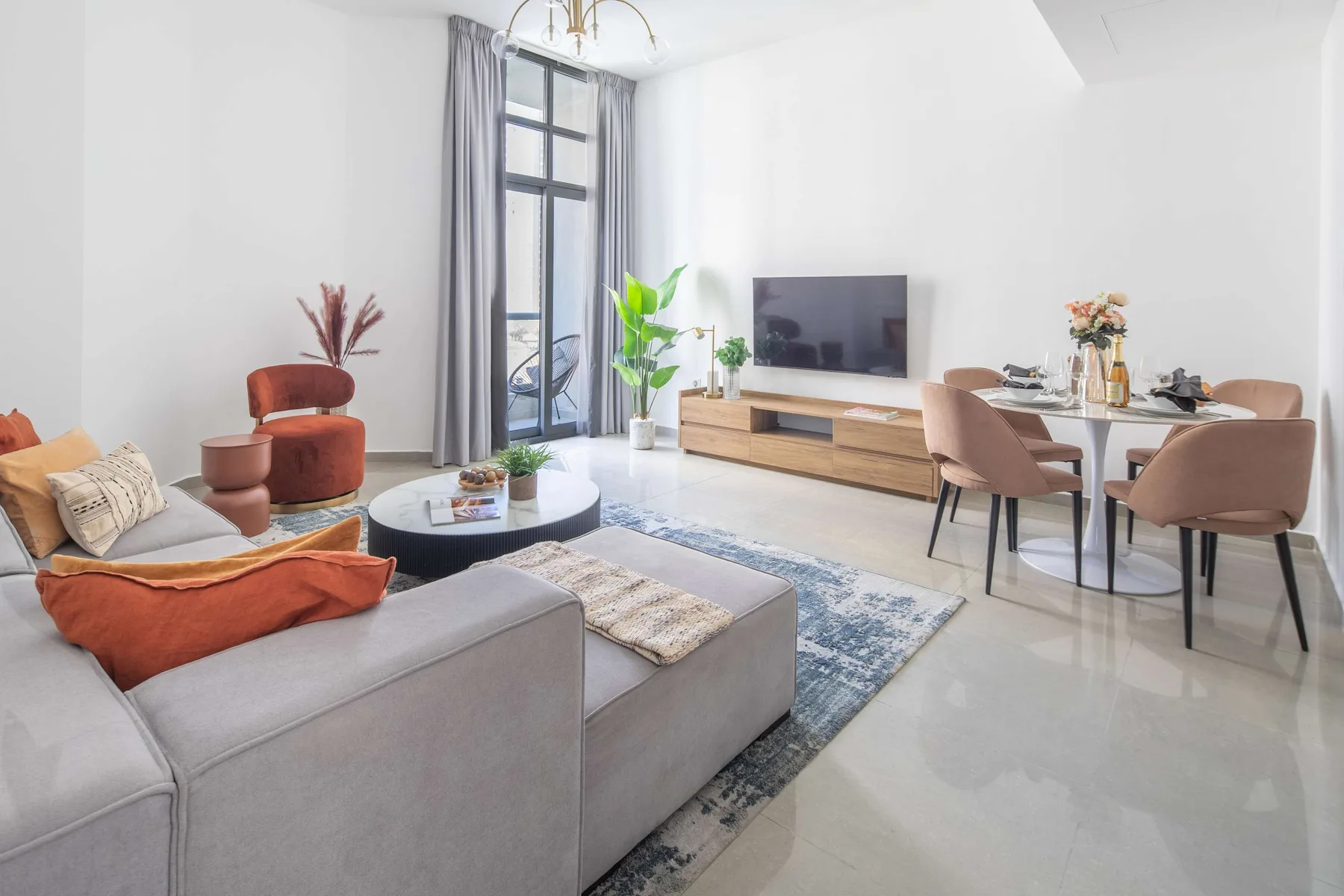 A bright living and dining area has seating, a television, and a tall window.