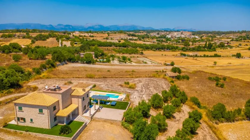 Aerial view of a house with a swimming pool amid open fields and scattered trees.