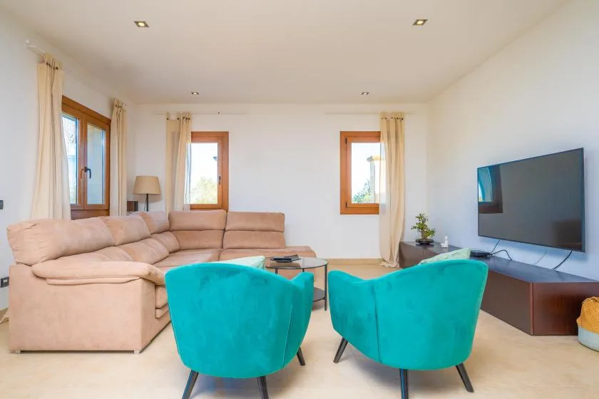 A bright living room with a beige sectional sofa, turquoise seating, and a television.