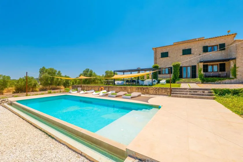 A swimming pool and paved patio sit in front of a modern house.