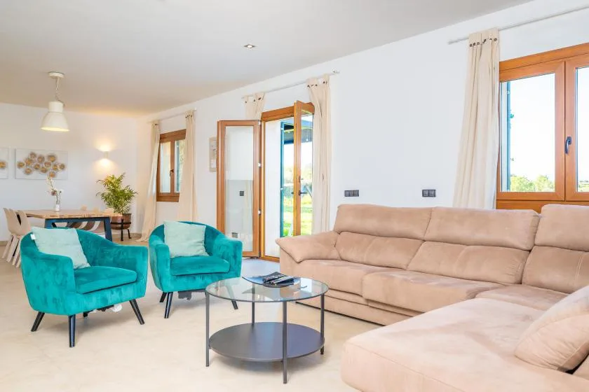 A bright living room with turquoise seating, a beige sofa, and a glass coffee table.
