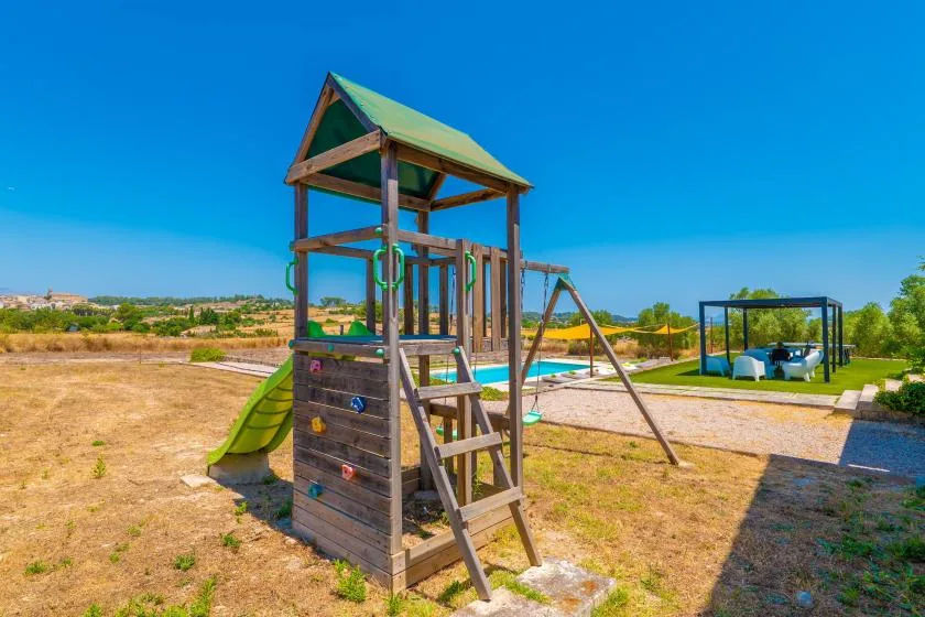 A wooden play structure with a slide stands in a sunny outdoor yard.