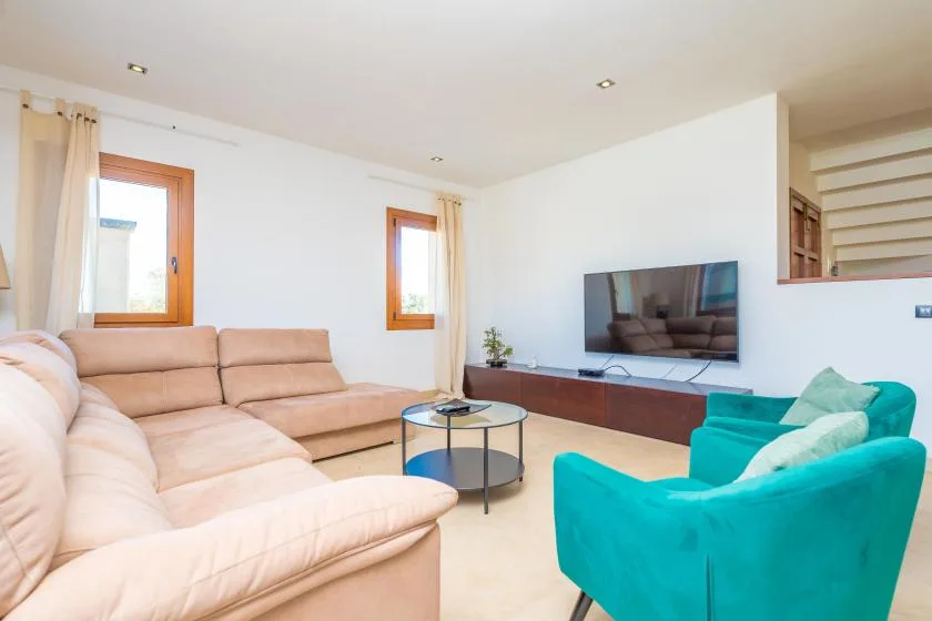 A living room with beige seating, a television, and a turquoise armchair.